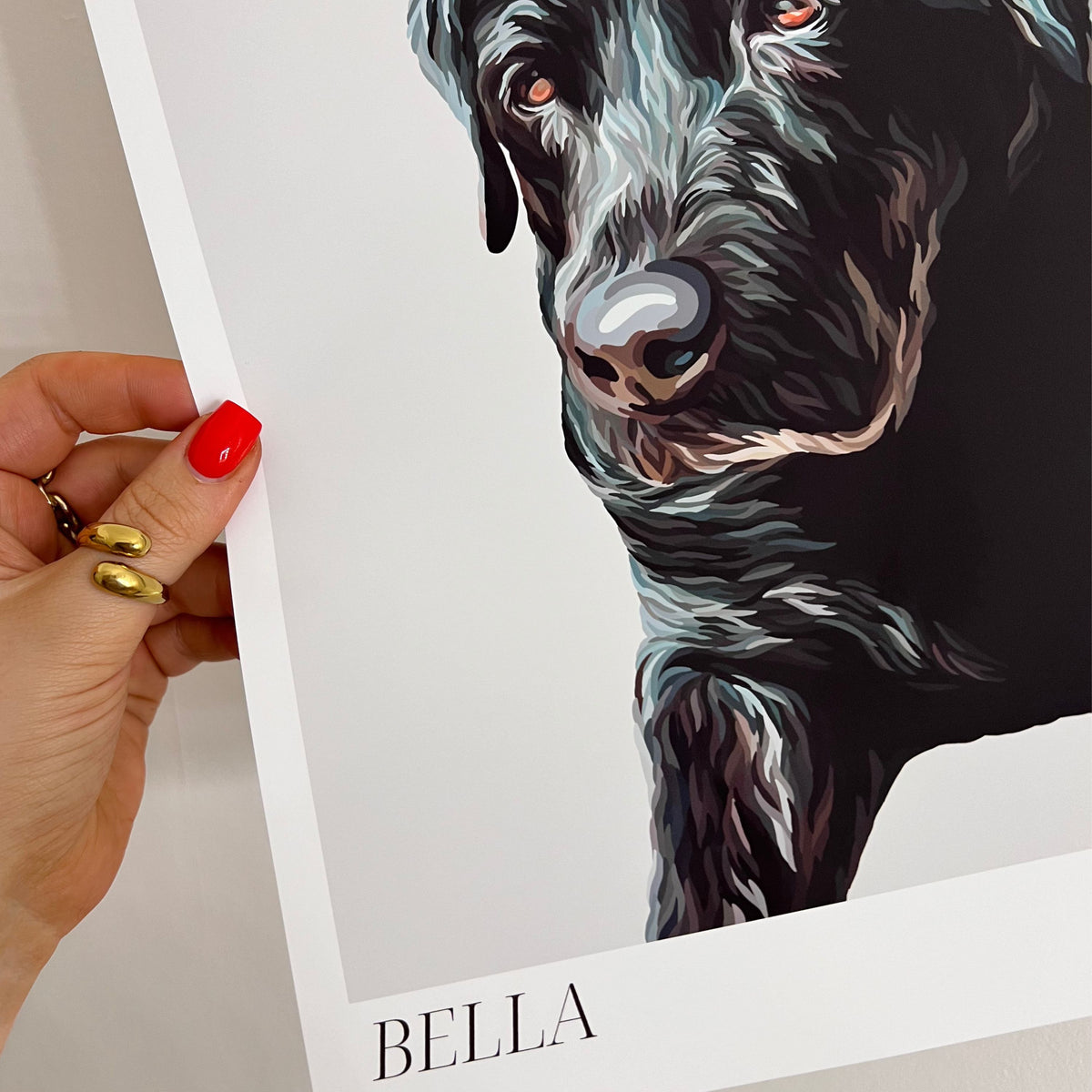 Hand holding a Bordered Detailed Pet Portrait print of a dog named Bella against a plain background.