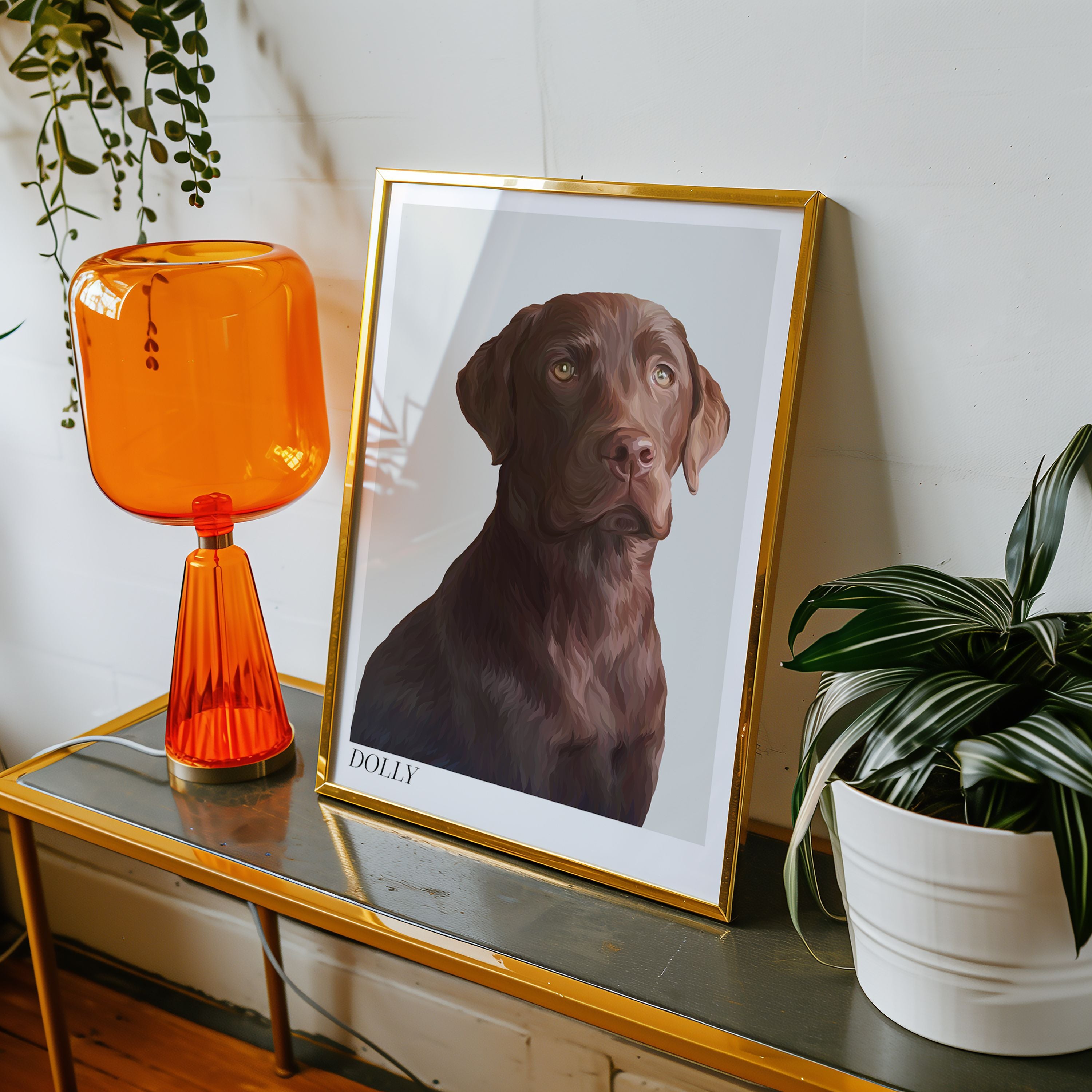 A framed Bordered Detailed Pet Portrait of a brown Labrador displayed on a table with an orange lamp and a plant in the background.