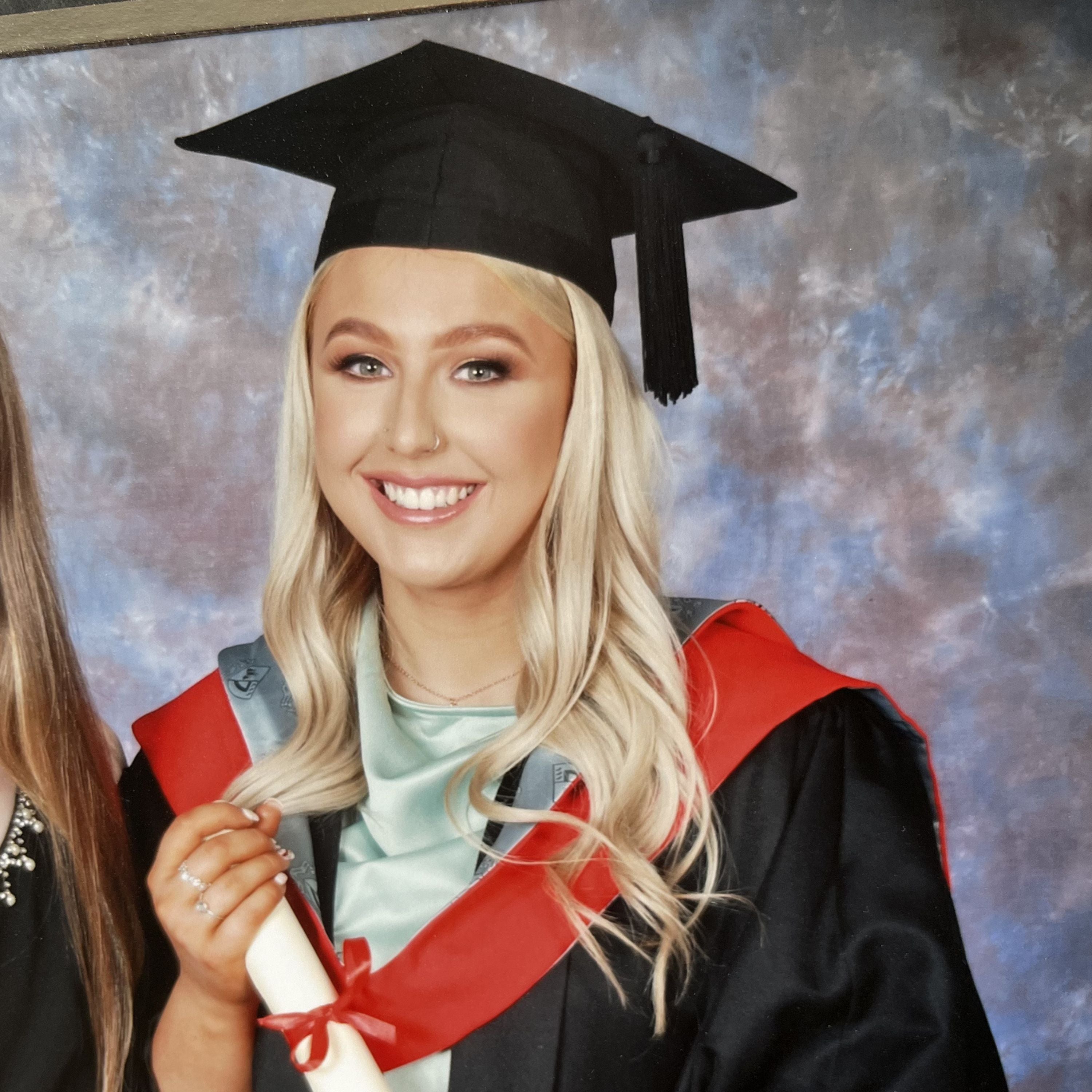 A girl smiling in a graduation gown and cap, holding her degree paper.