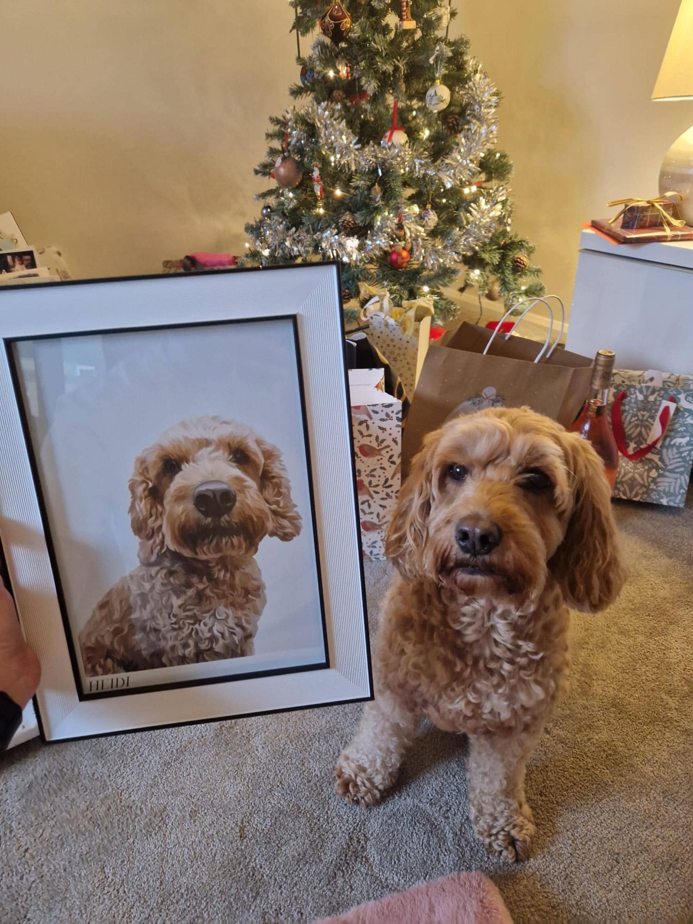 Dog sitting next to a framed Bordered Detailed Pet Portrait of itself in a living room with a Christmas tree behind.