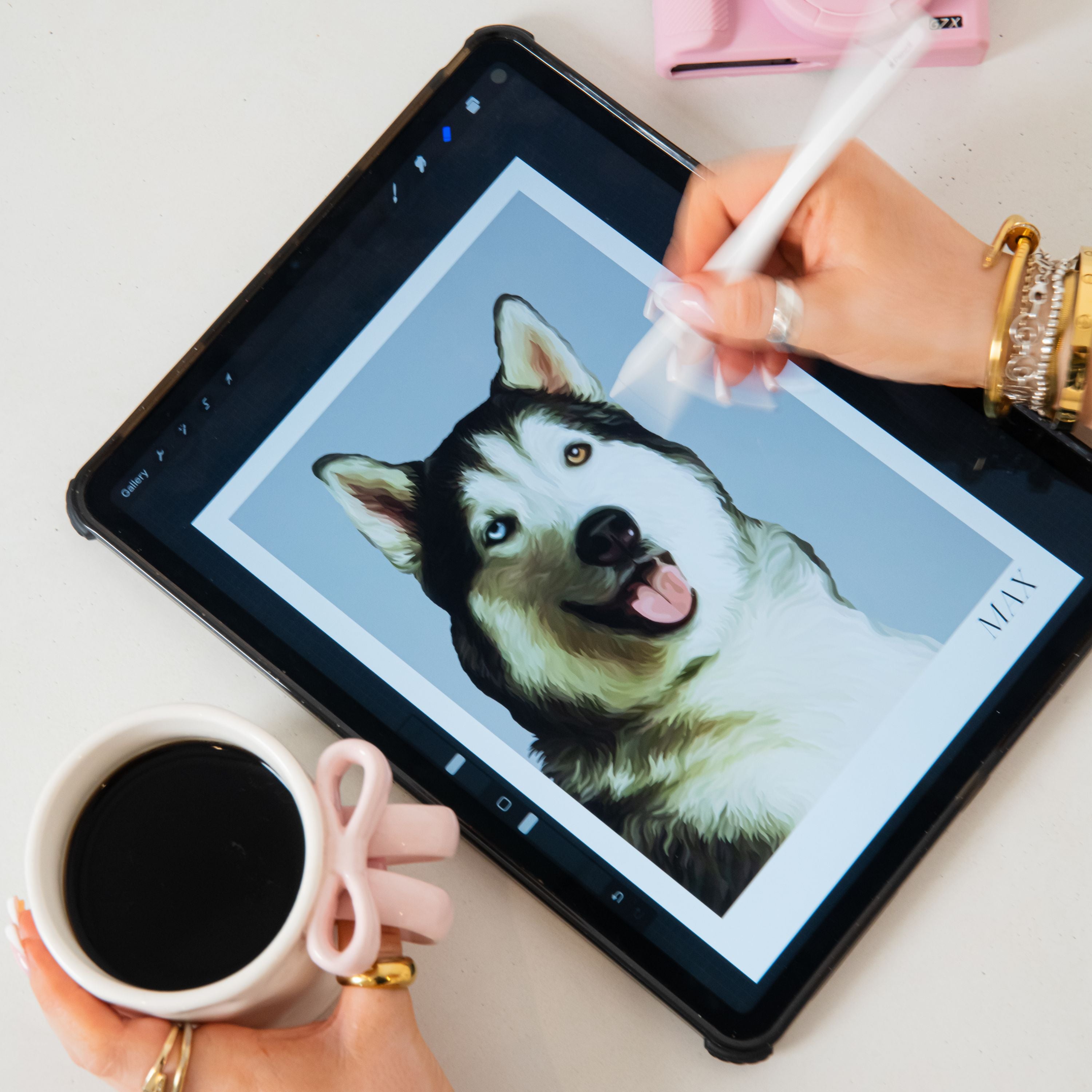 Person drawing a Husky dog on a tablet with a coffee cup and pink camera next to it.