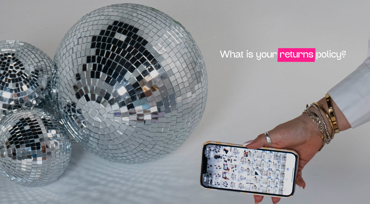 Three large silver disco balls on a white floor, with a hand holding a smartphone showing a snippet of a photo library and the text 'What is your returns policy?' on the right.